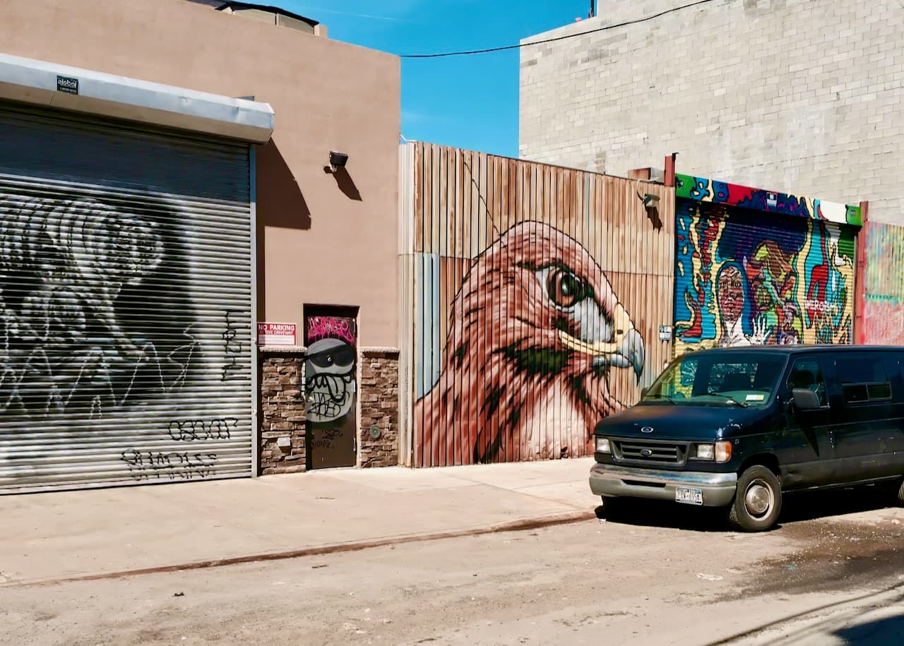 A street with colorful murals on garage doors and a parked van.