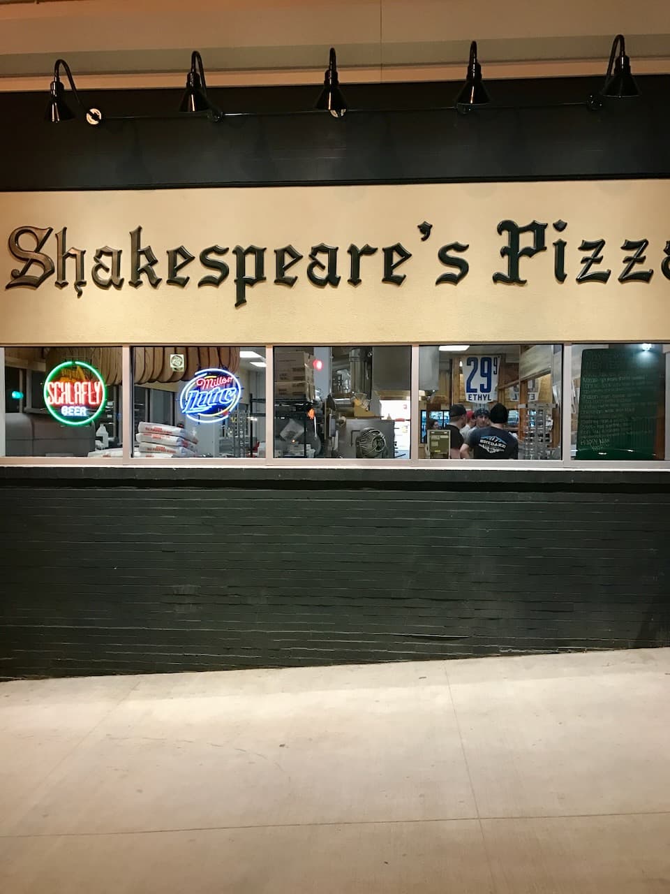 The Shakespeare's Pizza storefront at night with lit signs and kitchen windows.