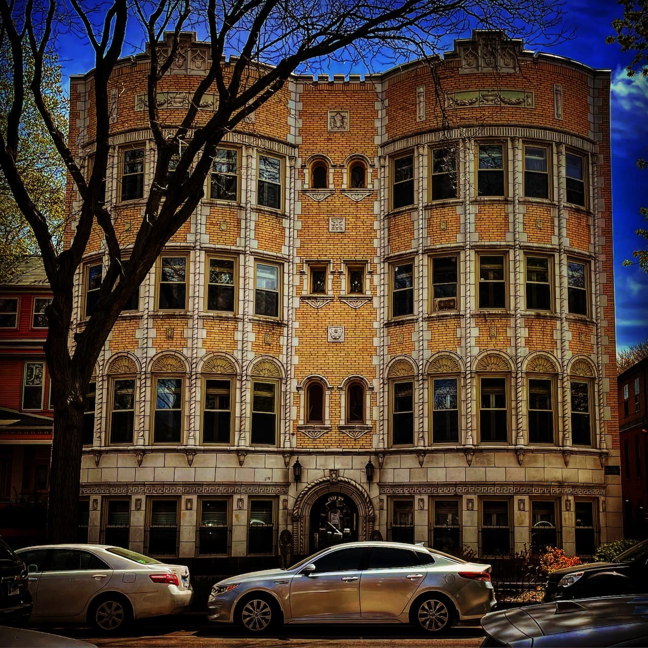 A detailed brick apartment facade with parked cars in front.