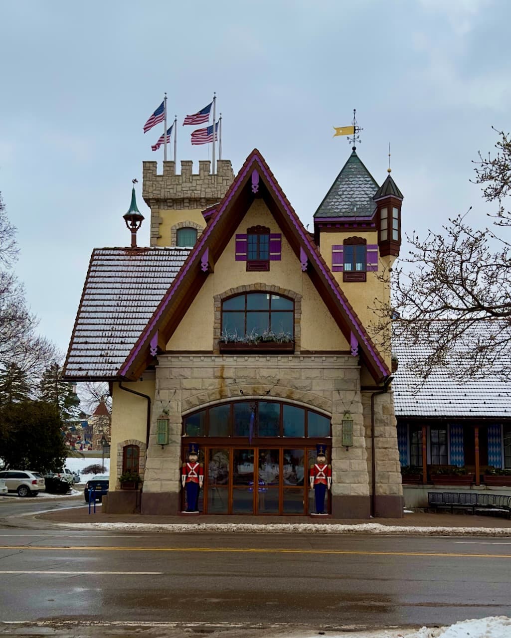 A Bavarian-style building with flags, painted trim, and snow along the street.