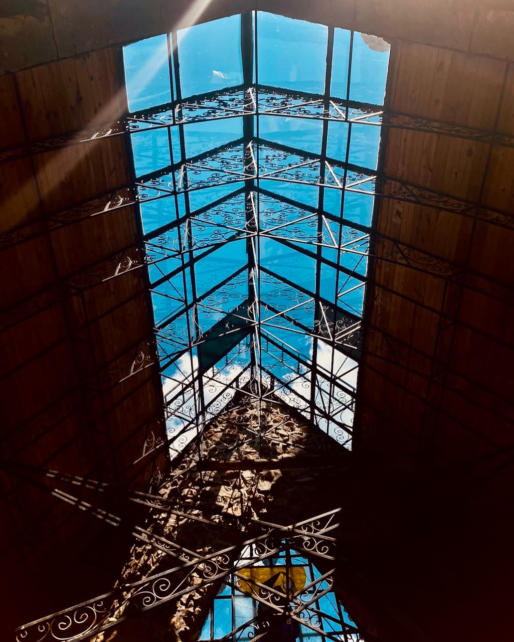 An interior view looking up through a blue glass skylight with ornate ironwork.