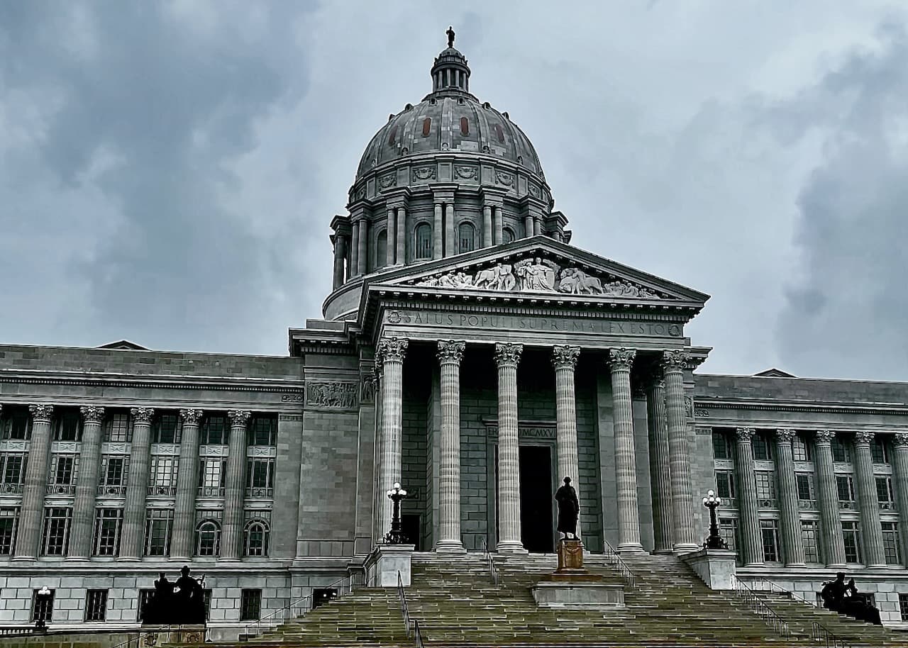 A domed civic building with columns and broad steps under gray clouds.