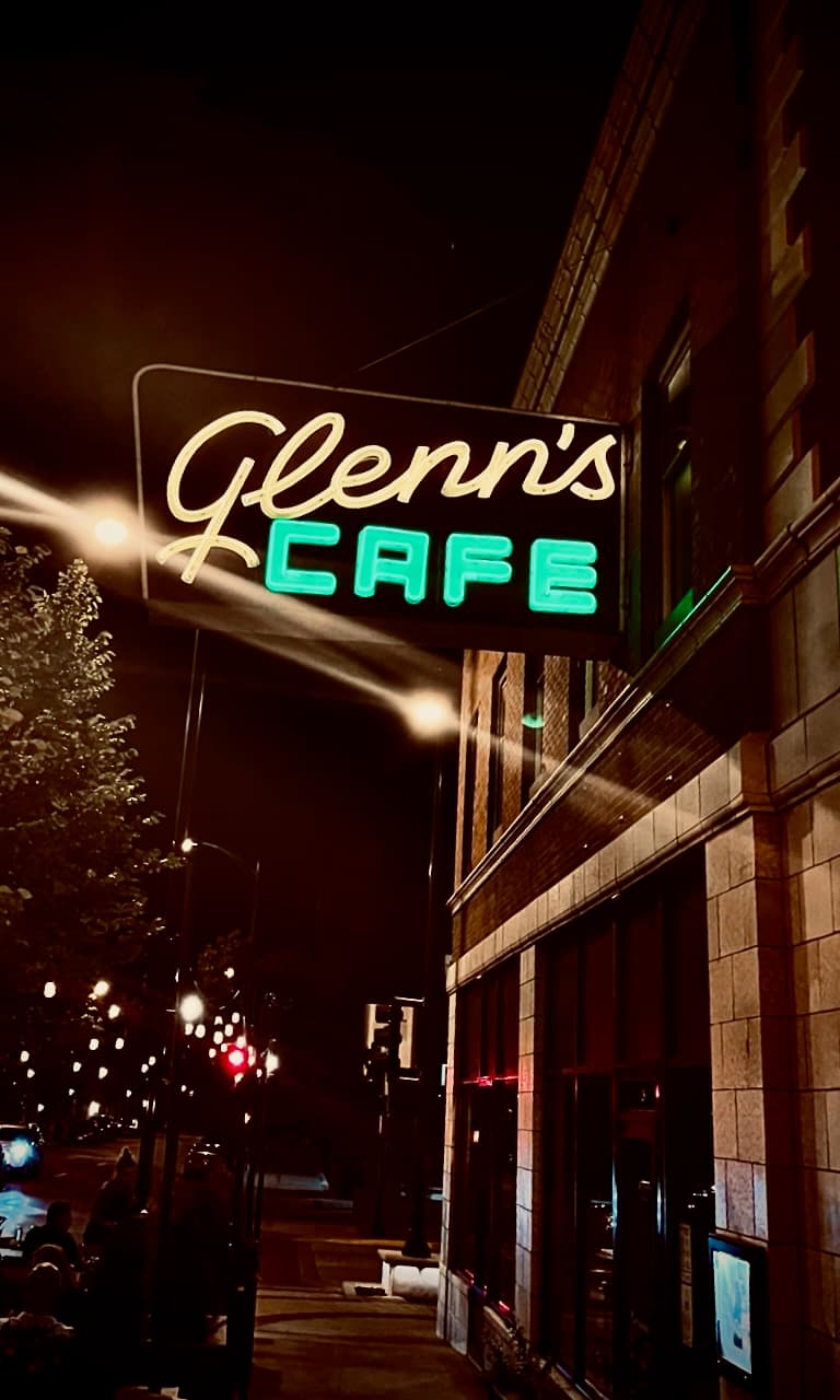 A glowing Glenn's Cafe sign at night above a city sidewalk.