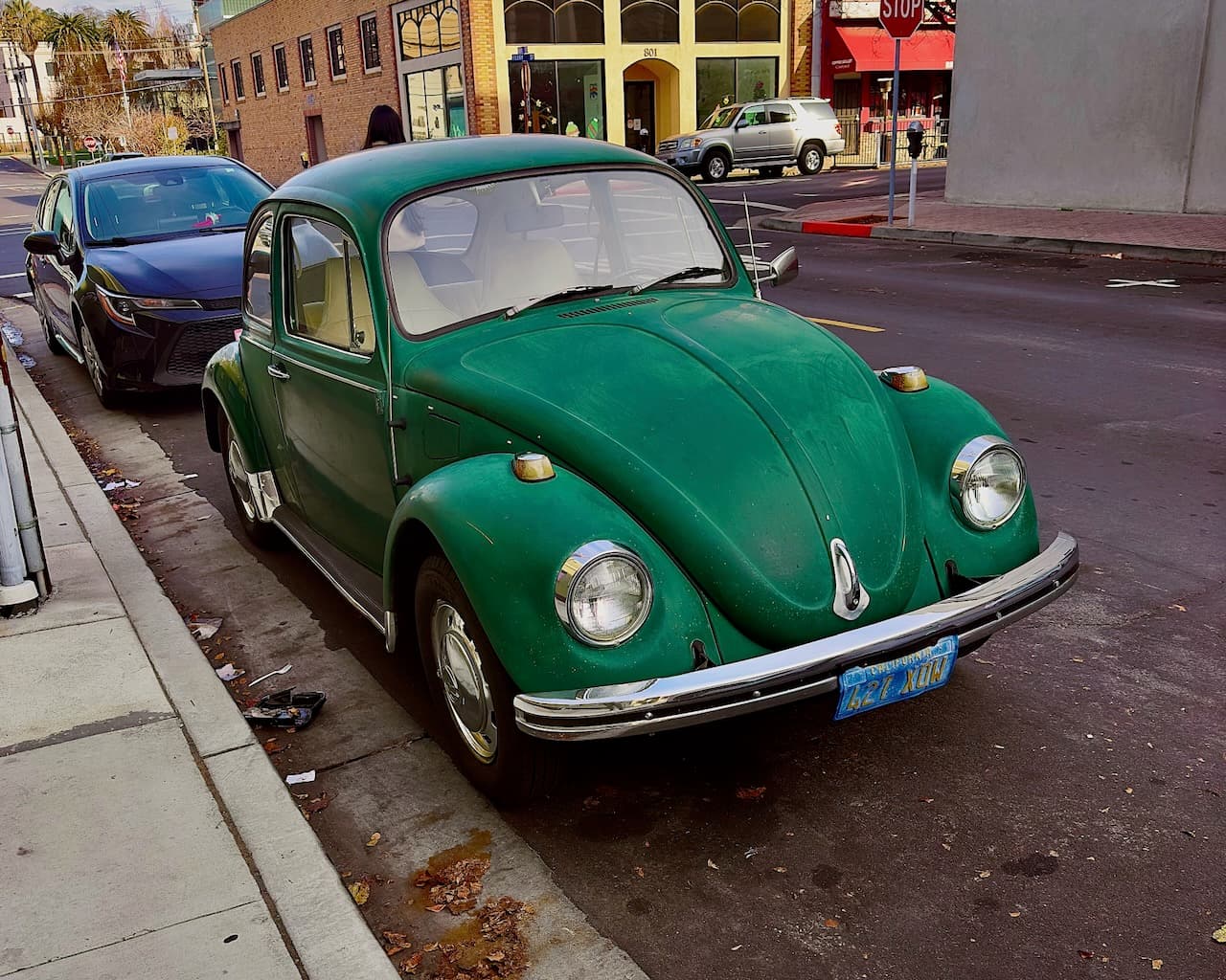 A green vintage Volkswagen Beetle parked on a city street.