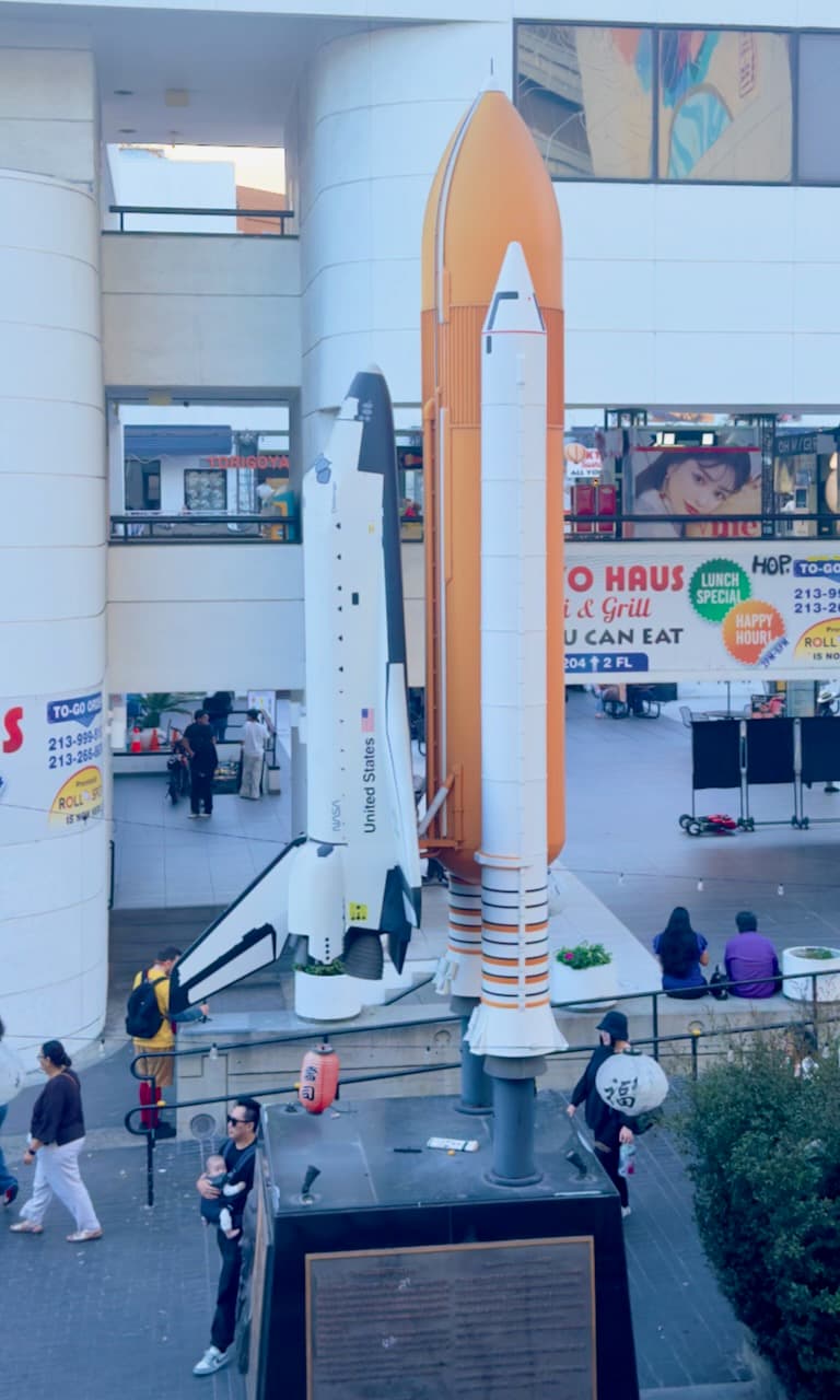 A model space shuttle and orange rocket boosters displayed in an open shopping plaza.