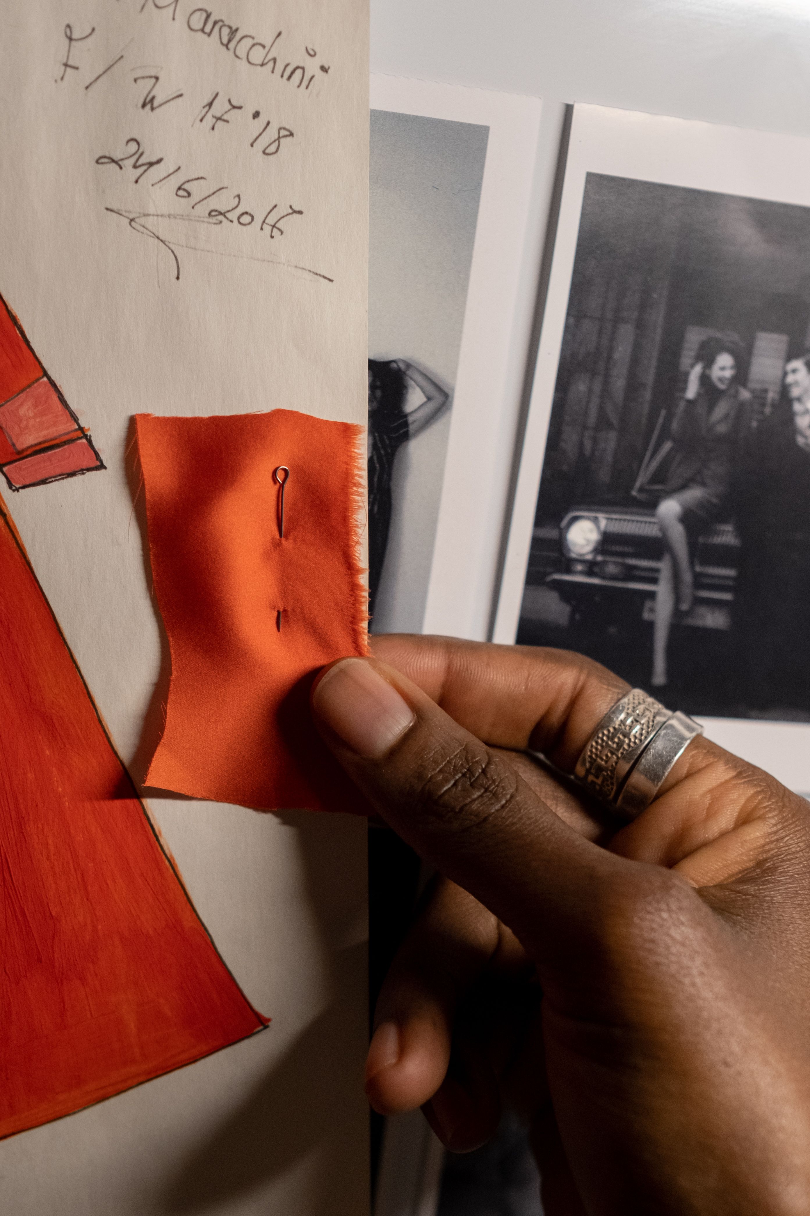 A hand pinning a fabric swatch beside research notes and photographs