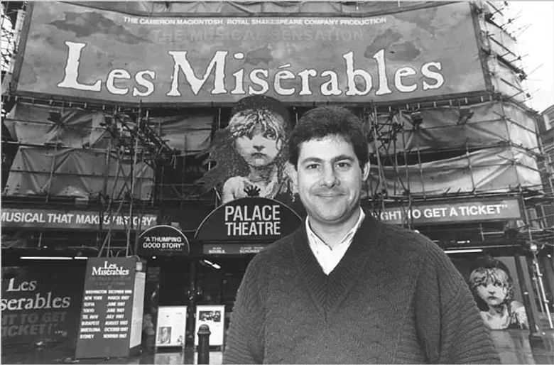 Archival portrait of producer Cameron Mackintosh in front of a Les Miserables sign.