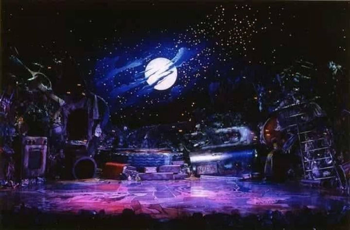 Scenic design image from Cats showing a theatrical environment with a large moon and layered stage elements.