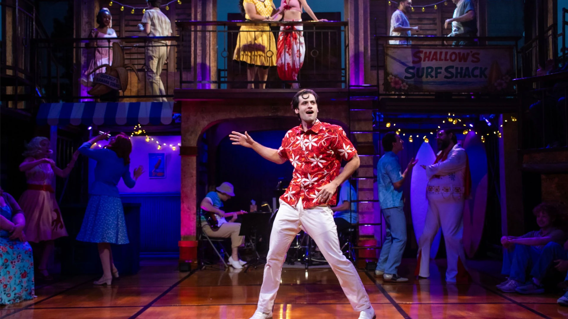 An ensemble musical number activates the colorful two-level surf-town setting for The Merry Wives of Windsor Cove at New Swan Theatre Company.