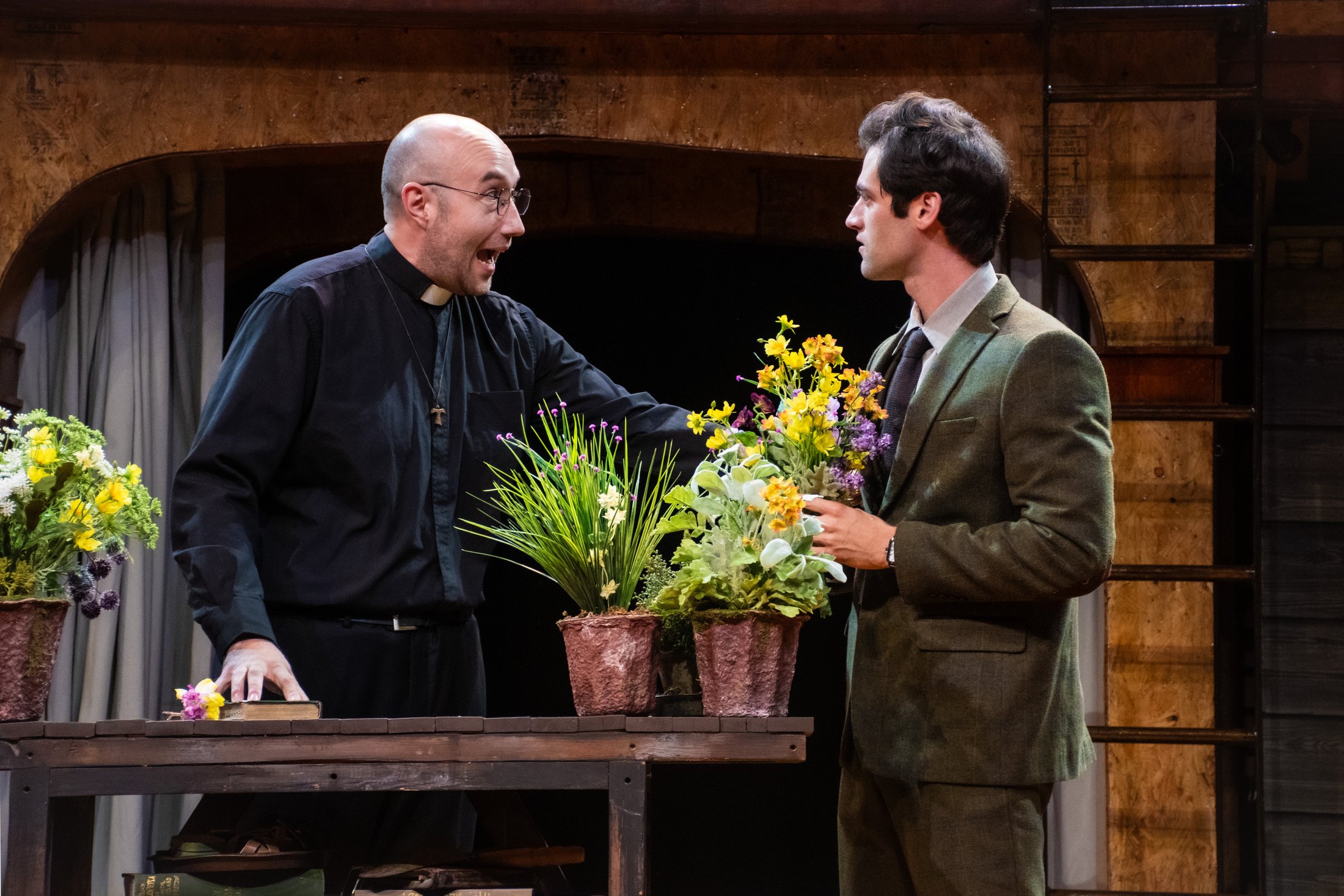 Friar Laurence speaks with Romeo beside a simple flower table.