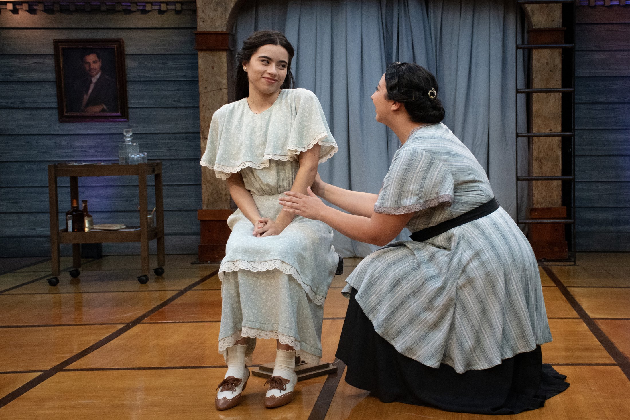 Juliet and the Nurse sit together against an open doorway and weathered timber walls.