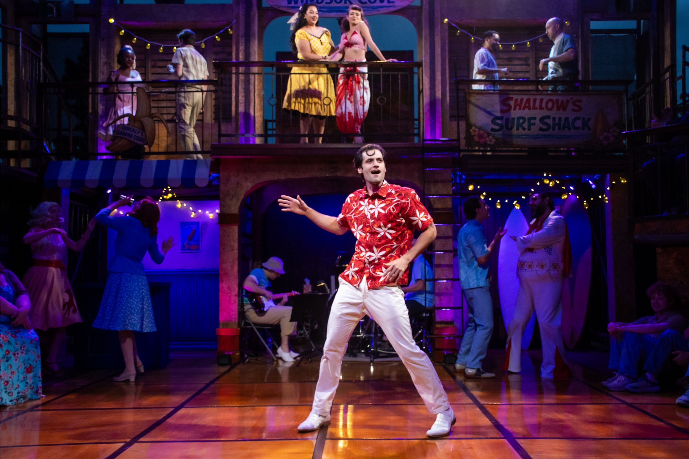An ensemble musical number activates the colorful two-level surf-town setting for The Merry Wives of Windsor Cove at New Swan Theatre Company.