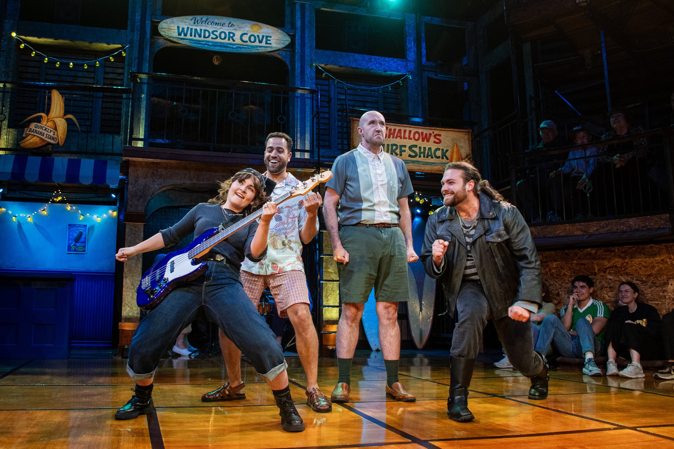 The ensemble gathers beneath the Windsor Cove and Shallow’s Surf Shack signs.