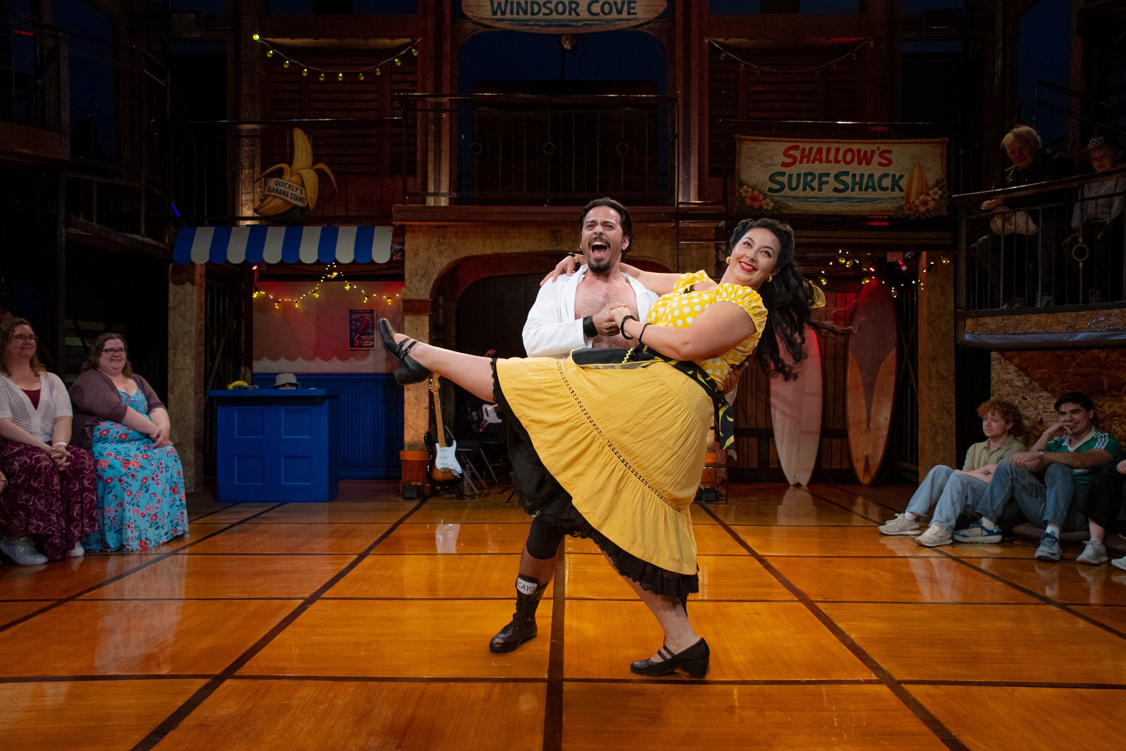 A dance lift crosses the open central floor of the in-the-round production.