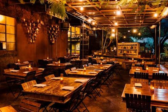 Covered Habana patio with warm string lights, wood tables, planting, and candlelit dining atmosphere.