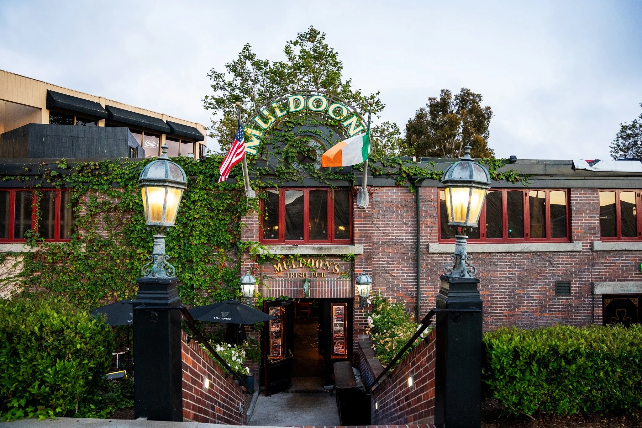 Exterior entrance to Muldoon's Irish Pub with ivy, brickwork, lanterns, flags, and pub signage.